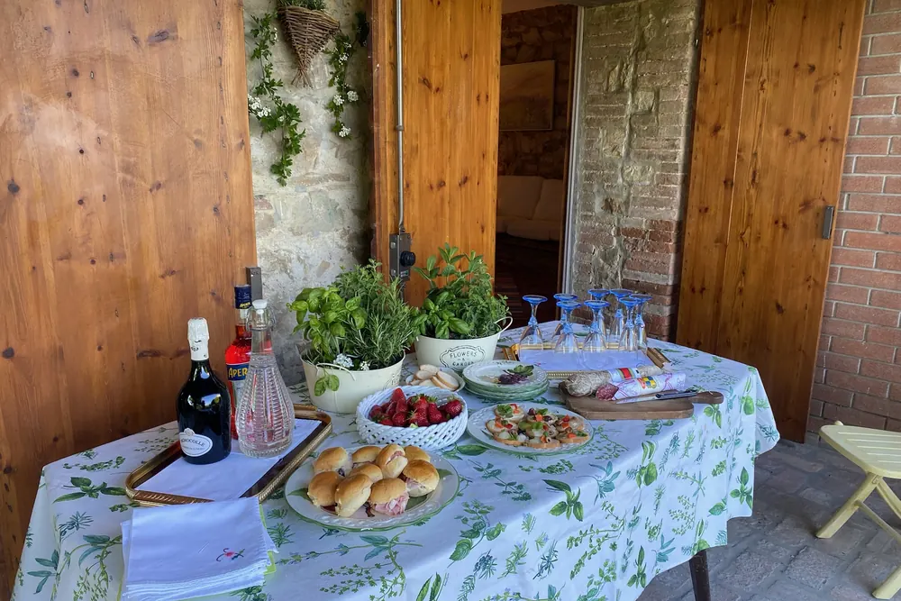 Tavolo apparecchiato per l'aperitivo sotto il portico in pietra, affacciato sul verde delle colline.
