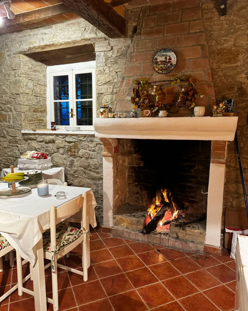 Angolo del camino la sera, con le fiamme che illuminano di calore la pietra e il legno della casa.