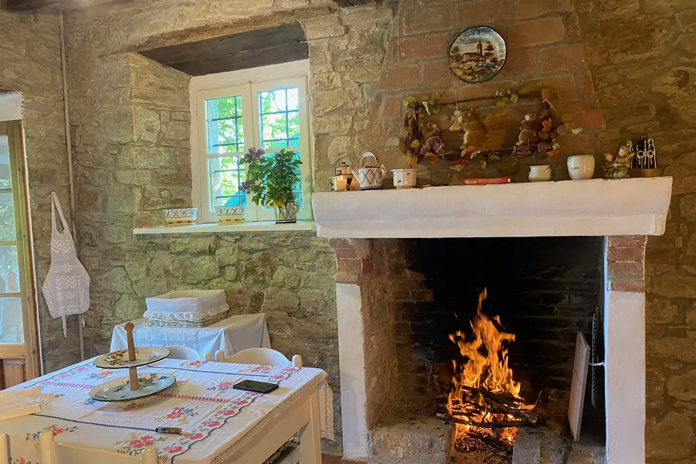 Camino di pietra acceso nel soggiorno rustico di Casa Urzano