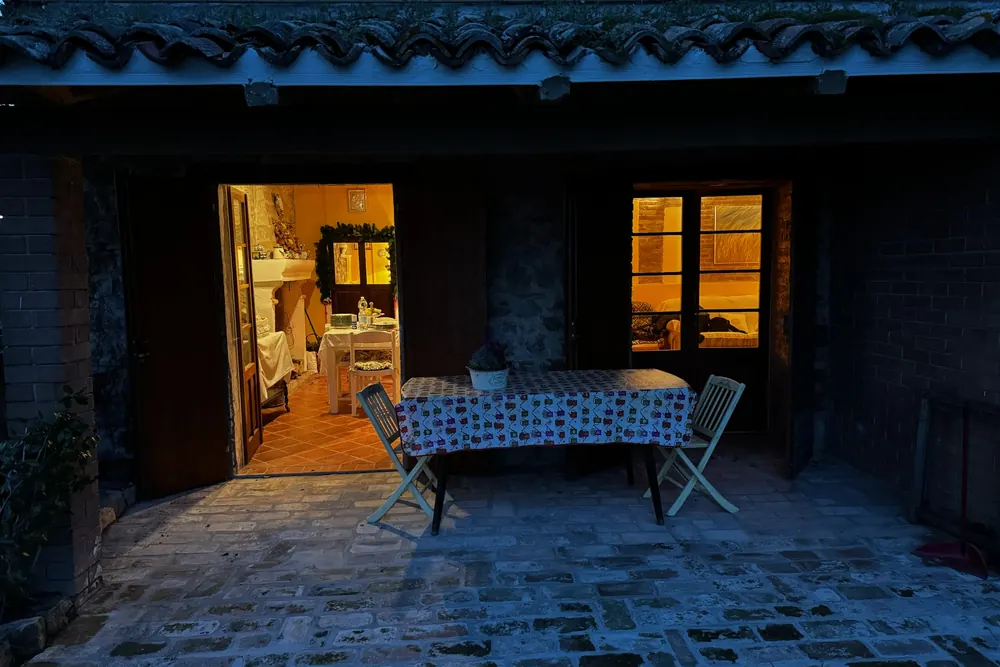 Il cortile in pietra della casa avvolto dalla luce blu del crepuscolo, con le colline che sfumano nel cielo della sera.