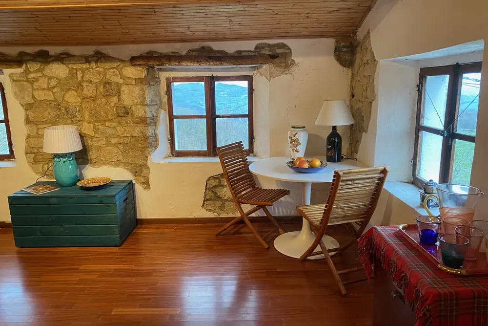 Stanza al piano superiore sotto le travi in legno, illuminata dalla luce naturale che entra dalle finestre affacciate sulle colline.